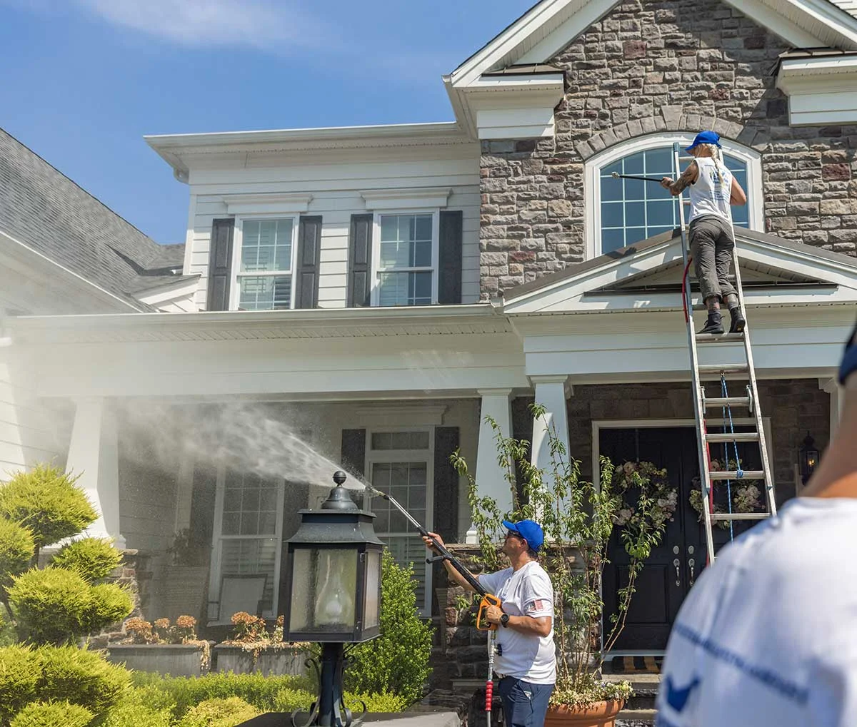 Professional team performing pressure washing on a large home exterior and porch to fully restore curb appeal