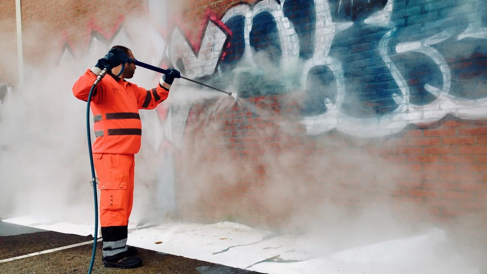 Professional steam graffiti removal service effectively cleaning old spray paint off a brick wall